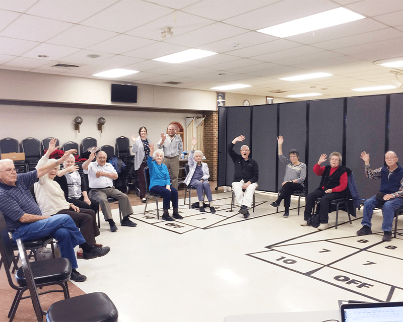 A group of older adults wave to the camera enthusiastically during a creative movement class