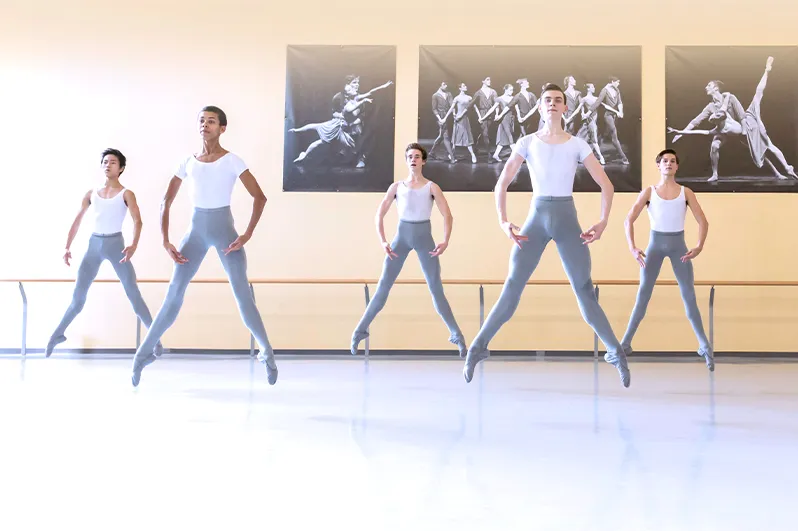Five dancers jumping in unison.