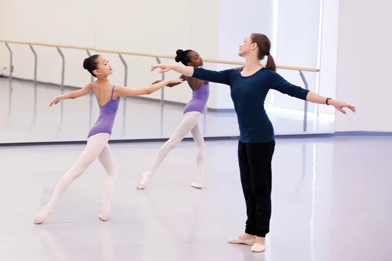 Une professeure dirige deux jeunes danseuses dans un cours de ballet