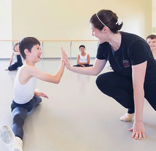 Un jeune danseur tape dans la main de sa professeure pendant un cours de ballet
